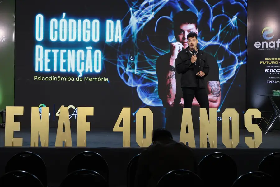 Bruno Scott no palco do ENAF 2026, com O Código da Retenção no telão